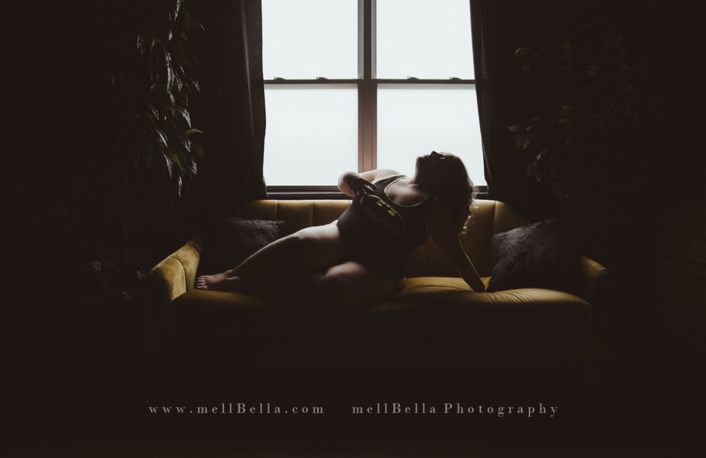 blonde woman in batman tank and panties stretching on yellow couch in front of window