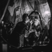 black and white image of a halloween styled room with spider webs, candles, a woman looking in a mirror, and a creepy shadow on the wall beside her