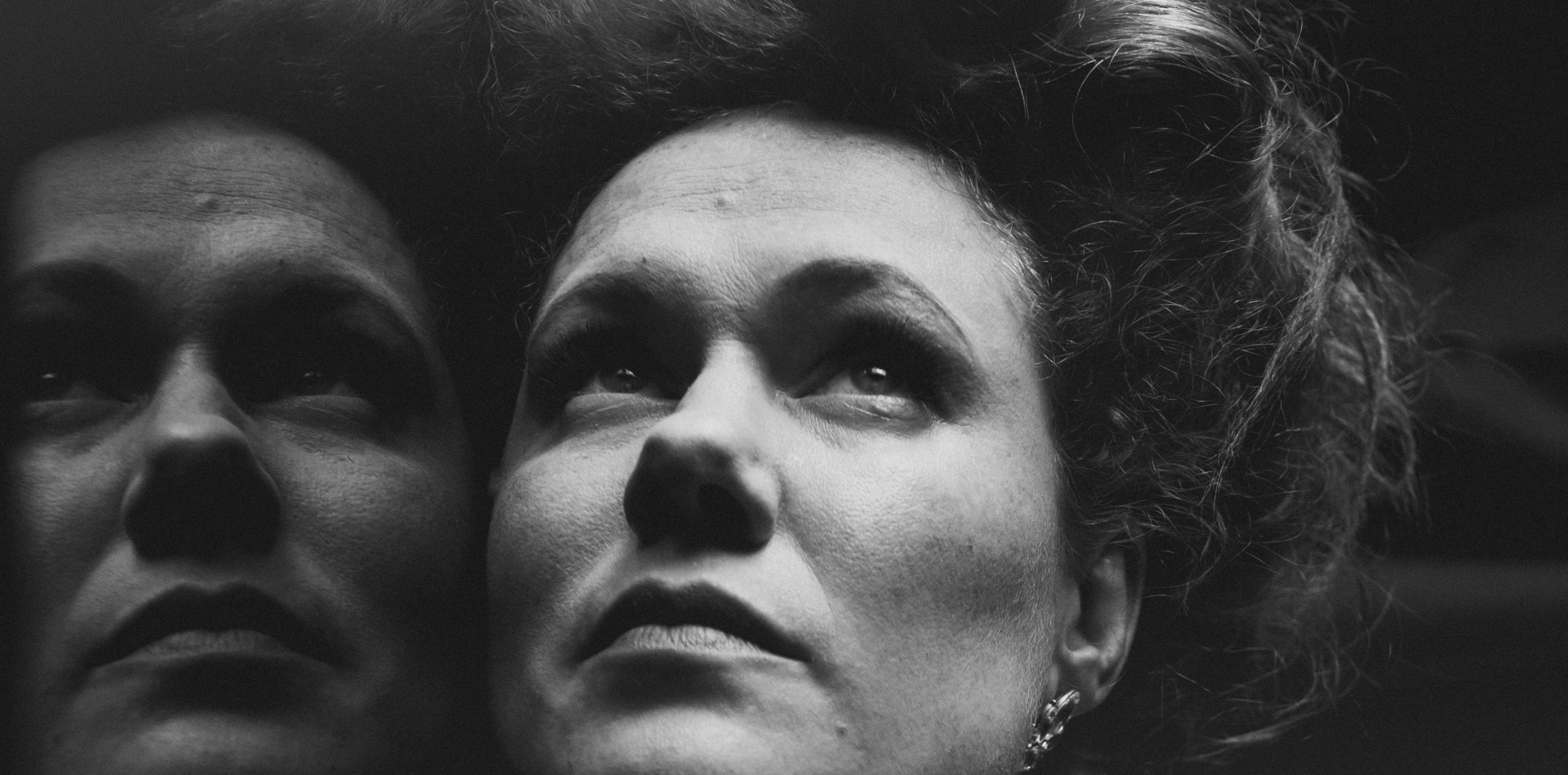 Black and White Close Up of a women's face with a reflection to the left. She has pale skin and freckles and her hair is in a 1910s style piled on top of her head. She is looking up with a pensive and somewhat serious look on her face.