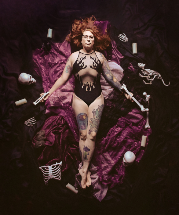 hallloween portrait of a woman laying on purple fabric surrounded by plastic bones and candles